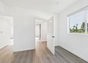 Thumbnail 18 of 22 - A room with white walls and wooden flooring with a door on the right.