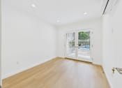 Thumbnail 20 of 28 - A room with a wooden floor and a sliding glass door leading to a balcony.
