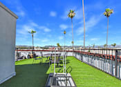 Thumbnail 20 of 23 - A rooftop patio with a green lawn, chairs, and palm trees.