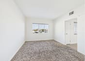 Thumbnail 23 of 33 - A room with a carpeted floor and a window showing a parking lot outside.