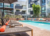 Thumbnail 32 of 35 - A pool area with sun loungers and umbrellas in front of a modern building.