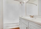 Thumbnail 7 of 17 - A white bathroom with a tub, sink and mirror.