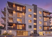 Thumbnail 1 of 20 - A modern apartment building with balconies and a person walking in front.