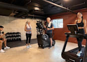 Thumbnail 18 of 20 - A woman is standing on a treadmill in a gym with other people around her.