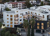Thumbnail 12 of 119 - A white building with black windows and balconies is surrounded by palm trees.