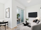 Thumbnail 32 of 163 - A modern living room with a white couch, a black coffee table, and a flat-screen TV mounted on the wall.