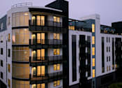 Thumbnail 113 of 163 - A modern building with black and white balconies is illuminated at dusk.