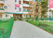 Thumbnail 17 of 17 - an apartment building with a green fence and a grey walkway leading to the front door