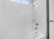 Thumbnail 46 of 66 - a white tiled bathroom with a tub and a window