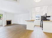 Thumbnail 35 of 60 - A spacious kitchen and living room with wood flooring and white walls.