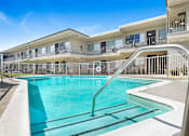 Thumbnail 1 of 6 - A swimming pool in front of a building with a metal railing.