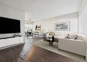Thumbnail 20 of 36 - A living room with a white couch, a wooden floor, and a flat screen TV mounted on the wall.