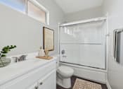 Thumbnail 23 of 36 - A white bathroom with a toilet, sink, mirror, and shower.