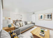 Thumbnail 22 of 50 - A living room with a grey couch, a wooden coffee table, and two framed artworks on the wall.