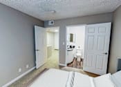 Thumbnail 20 of 34 - A bedroom with a bed in the foreground and a bathroom visible through an open door.