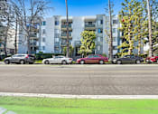 Thumbnail 79 of 95 - A street view of a residential area with cars parked on the side of the road and apartment buildings in the background.
