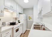 Thumbnail 1 of 15 - A white kitchen with a stove, sink, and refrigerator.