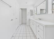 Thumbnail 24 of 29 - A white bathroom with a sink, mirror, and tiled floor.