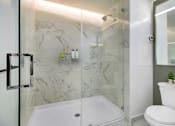 Thumbnail 10 of 31 - A white toilet sits next to a walk-in shower with a glass door.