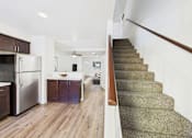 Thumbnail 3 of 34 - A staircase with a wooden handrail leads to a kitchen with a refrigerator and wooden cabinets.
