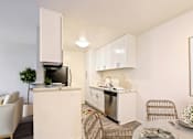 Thumbnail 8 of 33 - A modern kitchen with white cabinets and appliances, a dining table with chairs, and a potted plant.