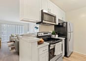 Thumbnail 9 of 33 - A black refrigerator is in a white kitchen with a stove and microwave above it.