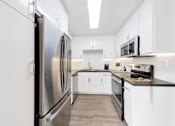 Thumbnail 1 of 19 - A modern kitchen with a stainless steel refrigerator and black countertops.