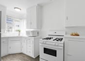 Thumbnail 10 of 26 - A white kitchen with a stove, oven, and microwave.