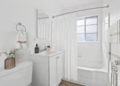 Thumbnail 19 of 26 - A white bathroom with a tub, sink, and mirror.