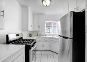 Thumbnail 1 of 26 - A black refrigerator stands in a kitchen with white cabinets and appliances.