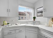 Thumbnail 2 of 26 - A kitchen with white cabinets and a window with blinds.
