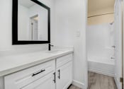Thumbnail 27 of 91 - A bathroom with a white vanity and a mirror.