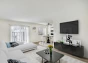 Thumbnail 3 of 95 - A living room with a white couch, a black coffee table, and a flat screen TV mounted on the wall.