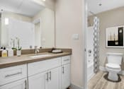 Thumbnail 19 of 26 - A bathroom with a white toilet and a sink with a mirror above it.