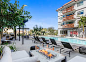 Thumbnail 1 of 64 - a pool with lounge chairs and a fire pit in front of a building