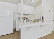 Thumbnail 15 of 46 - A white kitchen with a refrigerator, sink, and countertop.