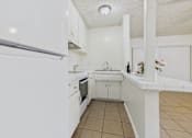 Thumbnail 25 of 46 - A white kitchen with a refrigerator on the left and a sink in the middle.