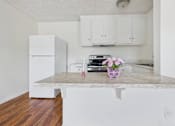Thumbnail 29 of 46 - A kitchen with a white fridge and cabinets, a marble countertop, and a wooden floor.