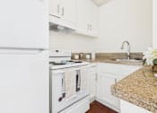 Thumbnail 16 of 46 - A white fridge and oven in a kitchen with a granite counter.