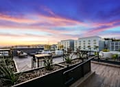Thumbnail 7 of 46 - A rooftop patio with a table and chairs overlooking a cityscape at sunset.