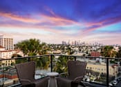 Thumbnail 8 of 46 - Two chairs and a table are set up on a balcony overlooking a city skyline.