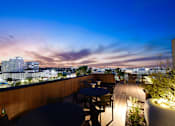 Thumbnail 9 of 46 - A rooftop patio with tables and chairs overlooking a cityscape at dusk.