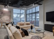 Thumbnail 3 of 46 - A living room with a large window, a couch, a coffee table, and a television at Skylar At Sunset Apartments, Los Angeles