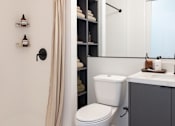 Thumbnail 37 of 46 - A white toilet sits next to a bathroom sink with a mirror above it at Skylar At Sunset Apartments, California, 90027