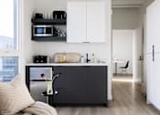Thumbnail 24 of 46 - A modern kitchen with white cabinets and a black fridge at Skylar At Sunset Apartments, Los Angeles, California