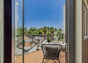 Thumbnail 7 of 157 - A chair is on a balcony with a view of a parking lot and trees.