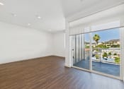 Thumbnail 35 of 45 - A room with a sliding glass door leading to a balcony with a view of a building and a palm tree.