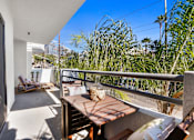 Thumbnail 6 of 54 - A balcony with a table and chairs overlooks a lush green area.