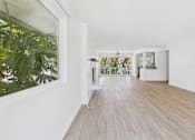 Thumbnail 7 of 251 - A long hallway with a white wall and a window with a view of a green plant.
