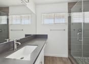 Thumbnail 9 of 251 - A modern bathroom with a large mirror, sink, and walk-in shower.